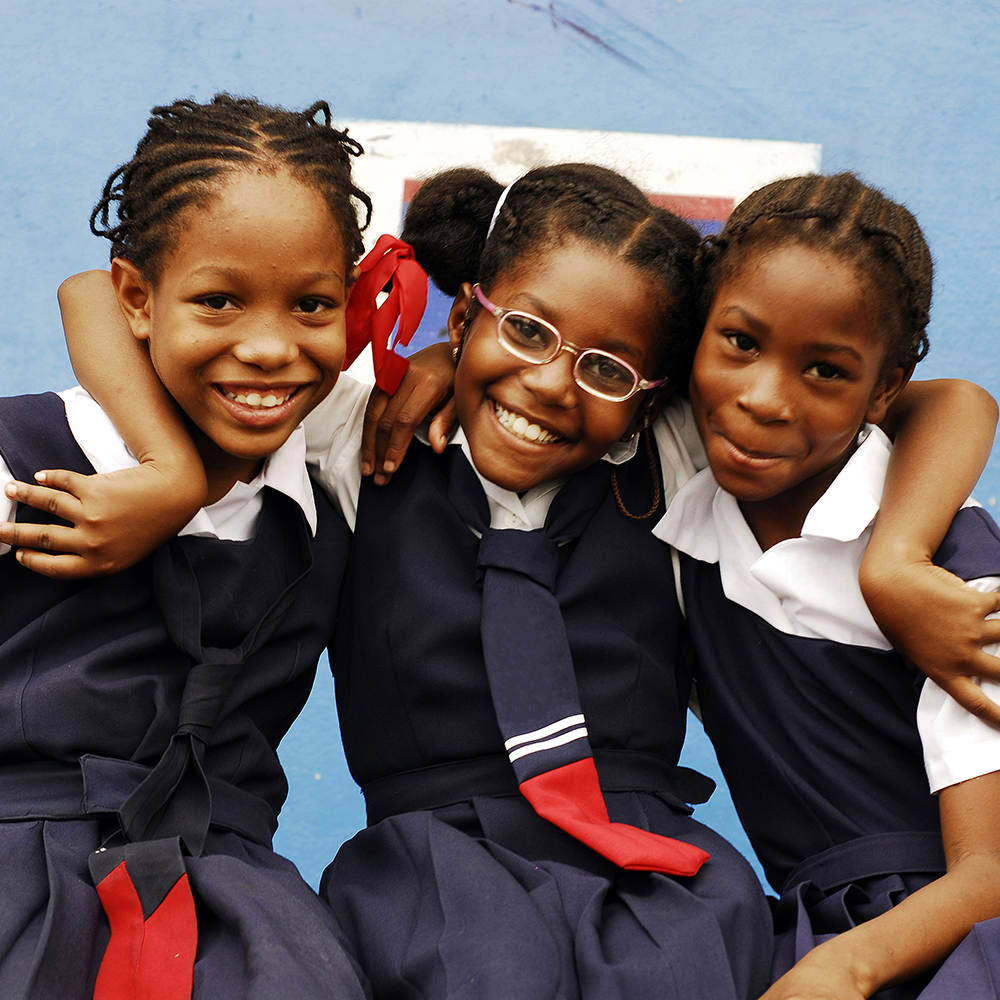 Three young school girls in uniforms smiling at the camera